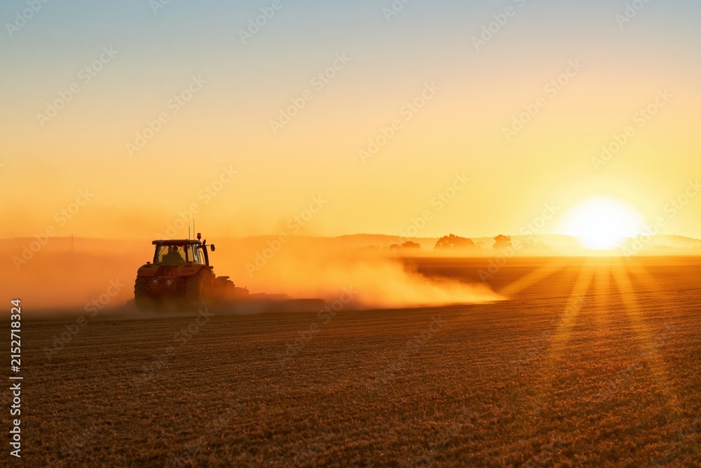 Obraz premium Agriculture tractor plowing field in rural countryside during a golden sunset