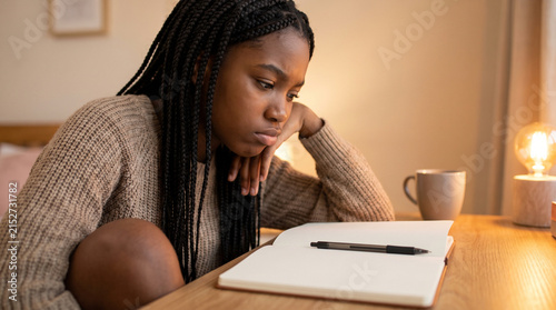 Sad young woman looking at blank notebook on desk