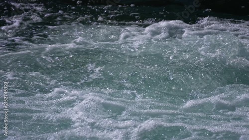 Water splashes and creates white foam across the turbulent surface of a fast flowing natural river.