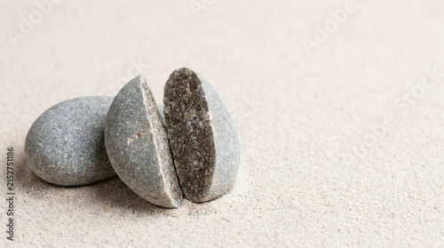 Two grey river pebbles on fine sand with one split cleanly in half
