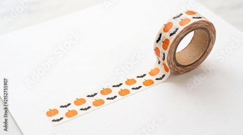 Washi tape with pumpkin and bat pattern rests on white paper for autumn scrapbooking and creative holiday craft projects in bright minimalist setting.