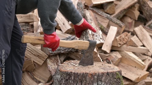 Man in red gloves chopping wood with an axe outdoors. Close-up of a man splitting a wooden log with an axe, symbolizing physical labor, energy, and fuel preparation