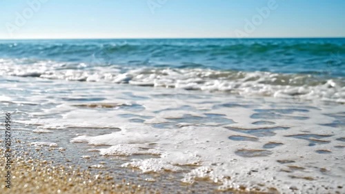 Ocean waves crashing on sandy beach shore under sunlight.