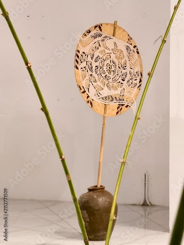 Traditional Asian Art: A rustic clay pot holds a bamboo stalk, supporting a delicate, circular fan adorned with intricate patterns, evoking a sense of timeless cultural artistry.