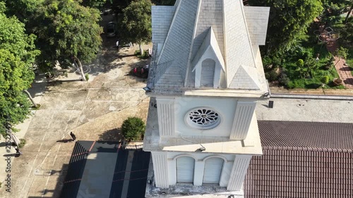 Drone footage beginning with a close view of the cross atop a church bell tower, then performing a descending orbit while the camera gradually tilts downward toward the ground.
