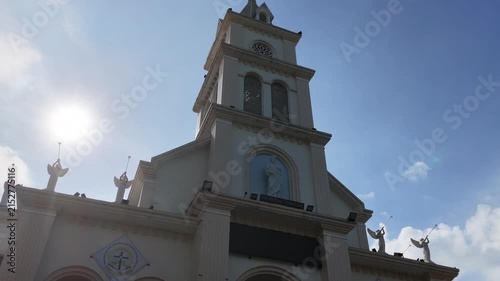 Drone footage orbiting a church bell tower while gradually ascending. The camera rises around the tower and progressively reveals the cross at its highest point
