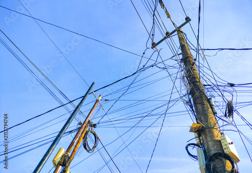 Messy Tangled Power Lines and Utility Poles Against Blue Sky