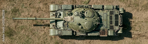 Military Tank Overhead View: An overhead shot showcases a military tank positioned on dry, grassy terrain, highlighting its robust structure and armament.