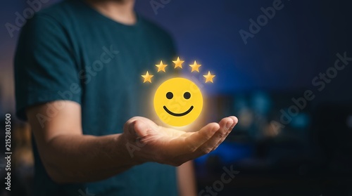 Customer satisfaction rating concept, man holding glowing yellow smiley face with five stars, excellent service feedback