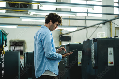 Printing Factory Employee Using a Tablet to Monitor Production Information and Manage Commercial Printing Operations Inside an Industrial Facility.  