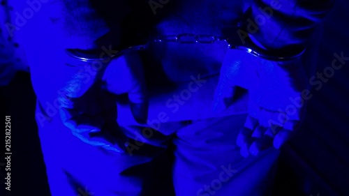 Handcuffs on hands under red and blue emergency vehicle lights.