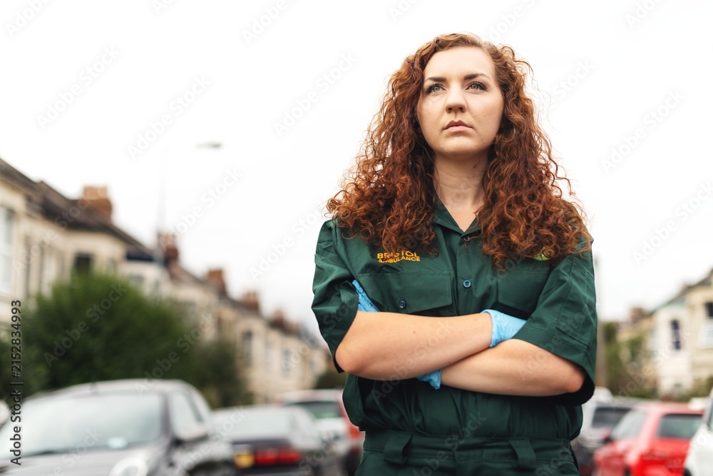 Fototapeta premium Person in green uniform stands confidently on a street with arms crossed.