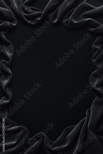 Dark silky fabric with smooth folds and subtle sheen framing black background, creating elegant composition with contrast of matte center and glossy textile texture.
