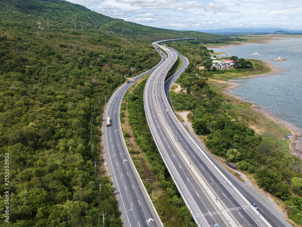 Obraz premium Drone aerial view of Motorway M6 Bang Pa-in–Nakhon Ratchasima expressway running beside Lam Takhong Reservoir in Nakhon Ratchasima, Thailand under cloudy skies