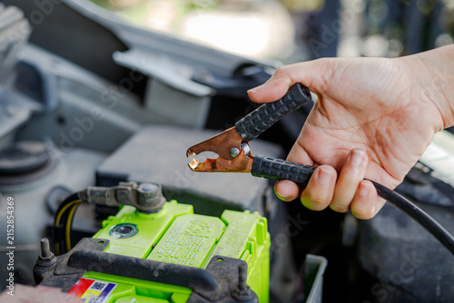 Hand holding jumper cable clamp near car battery