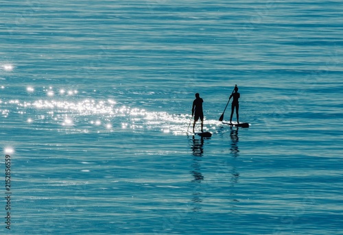 Canvastavla Two People Stand Up Paddleboarding on Sparkling Blue Ocean with Sunlight Reflect