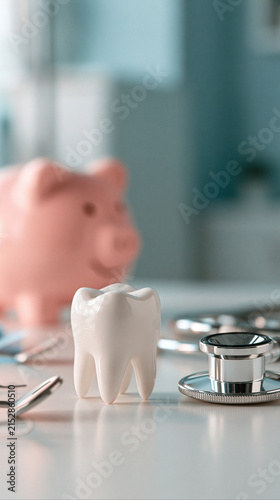 Dental Finance: A piggy bank and a ceramic tooth sit on a desk, next to dental instruments and a stethoscope, symbolizing dental care and saving for dental procedures.