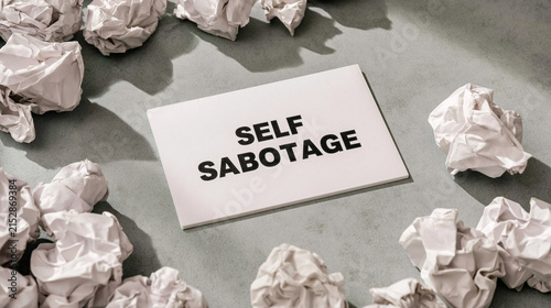 Self Sabotage: Crumpled paper balls surrounding a white card with the words SELF SABOTAGE highlight the theme of frustration, mental block, and creative struggle.
