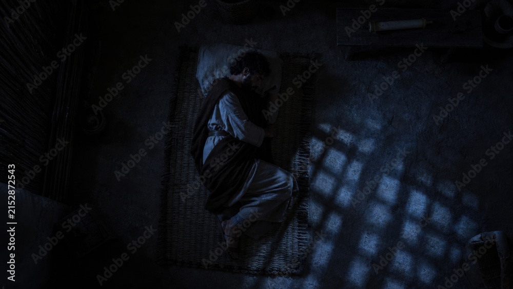 Obraz premium Joseph sleeping in a dark room. Biblical scene depicting man resting on a mat during the divine vision. Religious concept of the nativity story, faith, and spiritual guidance at Christmas.