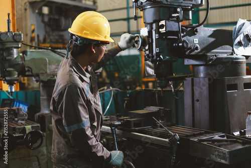 Фотография Professional Asian industrial worker operating a heavy drilling machine tool in a factory workshop