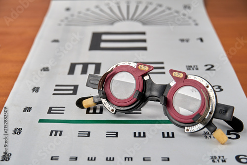 Optical trial frame with trial lenses on Snellen eye chart on wooden table