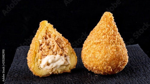 A crispy, deep-fried chicken coxinha with creamy curd cheese sits on a black paper towel against a black background