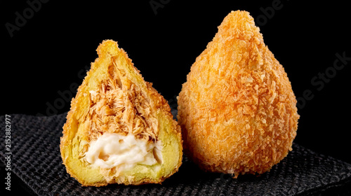 A crispy, deep-fried chicken coxinha with creamy curd cheese sits on a black paper towel against a black background