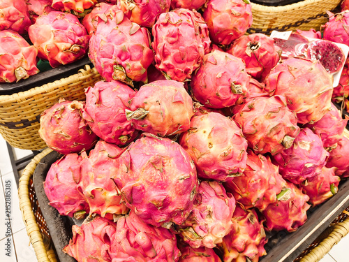 Bright pink dragon fruits pile high in woven baskets. Their scales glisten under warm market lighting. Vibrant colors draw attention to fresh, exotic produce. Ideal for food, health. No people present