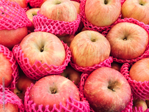 Bright red apples nestled in pink mesh bags. Fruits look fresh, smooth, and slightly shiny. Colorful packaging suggests a market or retail setting. Ideal for food, agriculture. Appeal evokes freshness