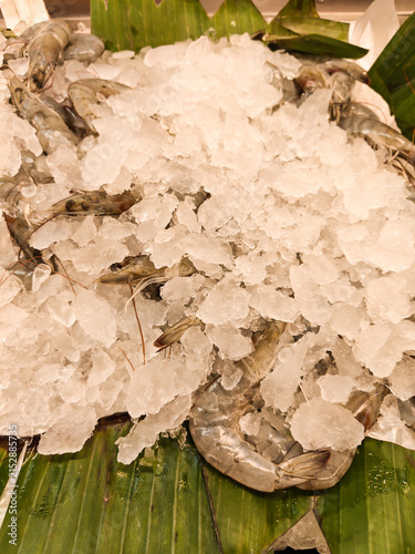 Fresh shrimp rest atop crushed ice on broad green leaves. Cool, crisp display invites seafood lovers and chefs alike. Market stalls and restaurant counters feature this vibrant setup
