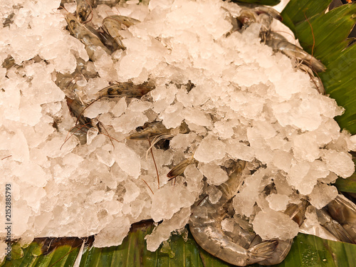 Fresh shrimp rest atop crushed ice on broad green leaves. Cool, crisp display invites seafood lovers and chefs alike. Market stalls and restaurant counters feature this vibrant setup