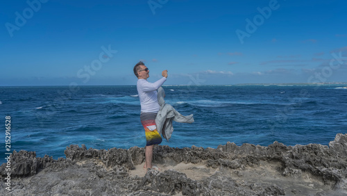 Fotografía A man stands on the rocky coast of a volcanic island, looks ahead, smiles, and raises his hand