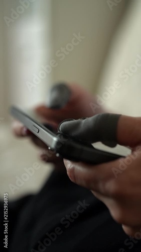 Person wearing gaming finger sleeves playing video game on smartphone, indicating intense mobile gaming session and using of specialized accessories for better performance and control, close-up.