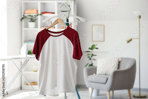 Fotografie White and maroon raglan t-shirt on a clothes steamer in a bright laundry room wi