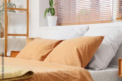Cozy bedroom interior with comfortable bed  soft orange and white pillows  and Wooden blinds on the window