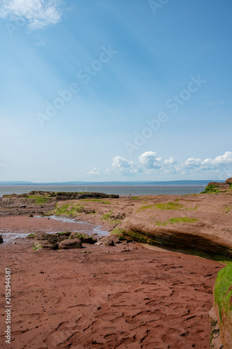 Low tide reveals red mud flats and sandstone cliffs under blue sky at Burntcoat Head Park, Nova Scotia.