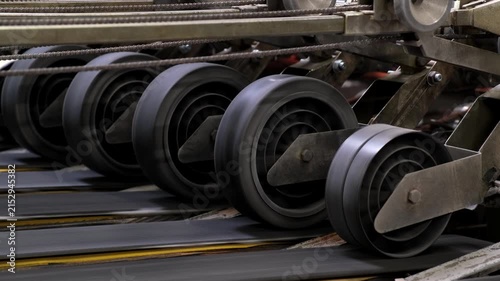 Detailed view of multiple rotating rubber rollers driving a transport belt mechanism inside an automated production plant.