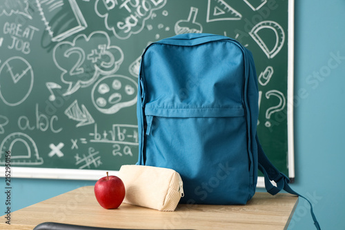 Backpack with pencil case and apple on desk in classroom