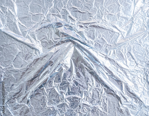 Detailed close up of shiny silver aluminum foil shows a heavily crumpled and wrinkled metallic texture creating an interesting abstract background