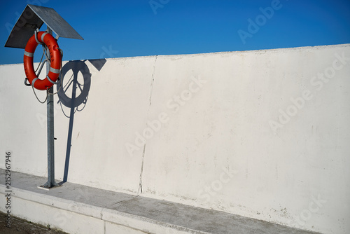 Orange lifebuoy mounted on metal post casting shadow on white breakwater wall, Marina Gdynia, Pomeranian Voivodeship, Poland, Europe