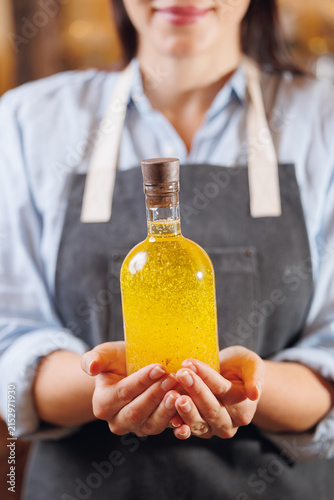 Konstfotografi Master woman in apron holds bottle with craft oil of sunflower with spices