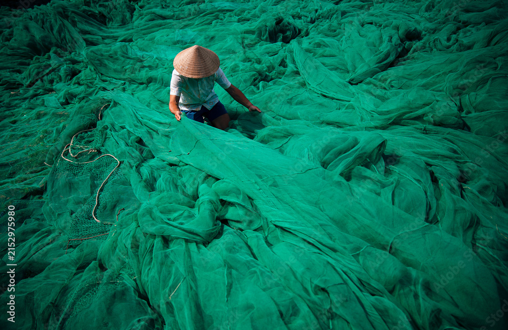 Naklejka premium Vietnamese fisherman with conical hat mending green fishing nets outdoors, traditional craft