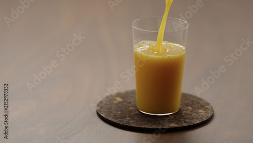Obraz na płótnie pour orange juice in a glass with ice cube on a wood table
