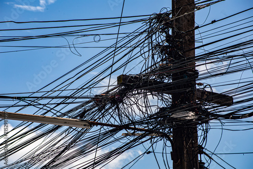 Bild auf Leinwand Chaotic Urban Power Lines and Tangled Communication Cables Against a Bright Blue