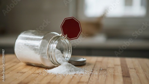 Tipped over salt shaker on wooden table with spilled salt