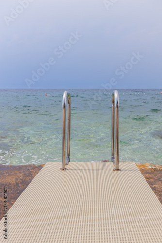 Stone seaside platform with ladder leading into calm Adriatic waters in Croatia coastal setting