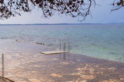 Stone seaside platform with ladder leading into calm Adriatic waters in Croatia coastal setting