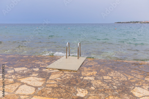 Stone seaside platform with ladder leading into calm Adriatic waters in Croatia coastal setting