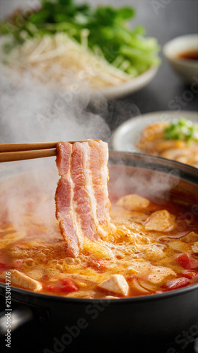Hot soup with tofu and pork slice held by chopsticks steaming