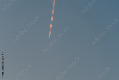 Bild auf Leinwand Airplane contrail streaking across a clear blue sky during sunset, creating a vi